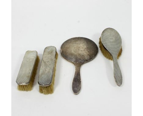 A part silver-backed dressing table set comprising a hand mirror, lint brush and clothes brush, each with engine turned desig