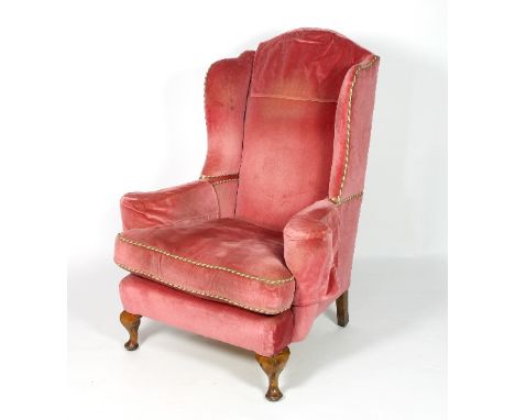 A pink velvet upholstered wingback armchair with striped cord trim and loose seat cushion, on turned legs