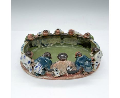 Ten figures delicately hold onto the sides of this handmade oblong ceramic bowl, featuring a multi-colored glaze. Dimensions: