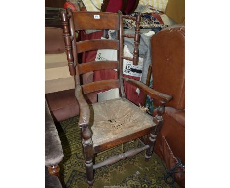 An antique high ladder back open armed Armchair having a distressed rush seat, standing on turned front legs and the back wit