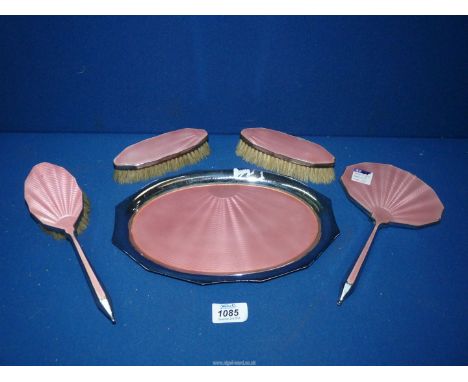A vintage dressing table set in pink enamel comprising tray, two clothes brushes, hairbrush and hand mirror.