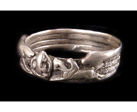 A vintage Anglo-Indian white metal bangle, modelled as a coiled snake and having a tiger and horse and rider