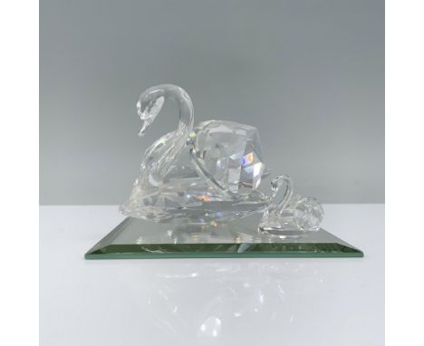 Two clear crystal swans gracefully swim with their wings at their backs, elegantly joined by a square mirror base. Swarovski 
