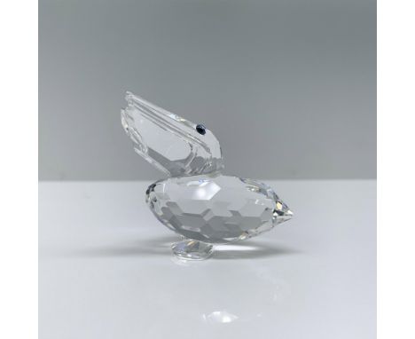 A clear crystal pelican that is sitting down with its head slightly raised and turned, accented with melon colored crystal ey