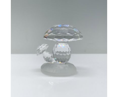A small clear crystal mushroom, featuring hexagonal cuts on the cap, delicately rests upon a frosted glass base. Swarovski ba