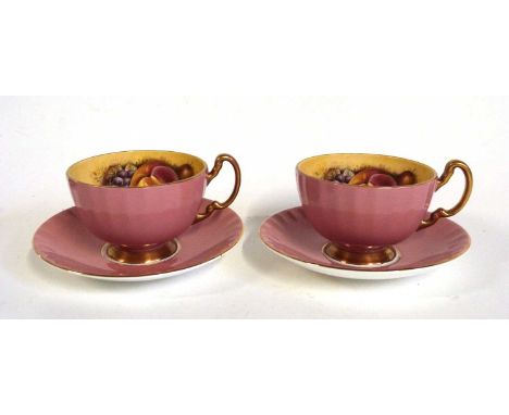 Two Aynsley cups and saucers with pink exterior ground, the interior printed with fruit