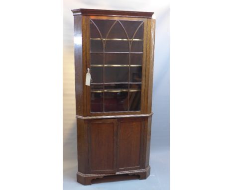 An early 20th Century oak corner cabinet with glazed door above two cupboard doors raised on carved bracket feet