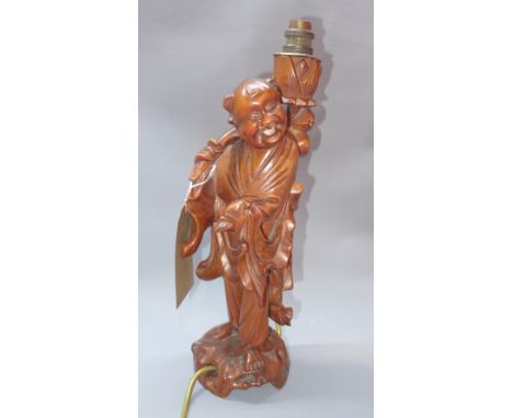 A Chinese carved hardwood figural table lamp in the form of a traveller, raised on naturalistic base, H. 43cm