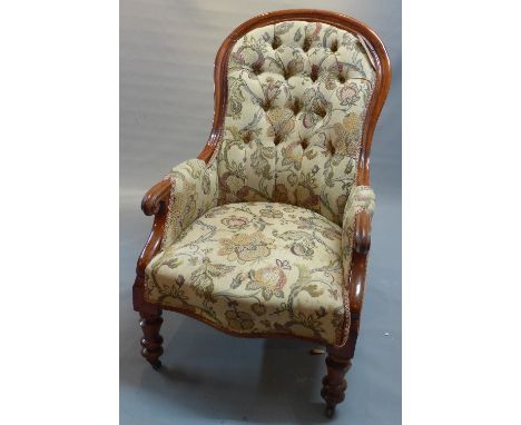 A Victorian mahogany spoon back armchair with scroll arms, floral button back upholstery raised on turned legs and castors