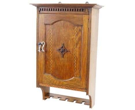 An Edwardian oak smoker's cabinet, the over run top raised above a dentil frieze and carved door, with an ebonised and boxwoo