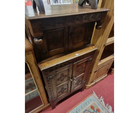 A contemporary joined and relief carved oak compact court cupboard, having an arrangement of four cupboard doors and a brushi