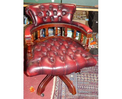 A contemporary mahogany burgundy red leather buttoned upholstered and further brass studded tub swivel desk chair, raised on 
