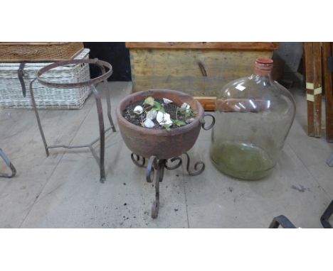 A terracotta planter on stand, a carboy and a metal stand 