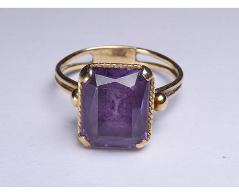 A Romanesque amethyst ring - the emerald cut stone claw set on a raised rope-twist setting, size V, 6g.
