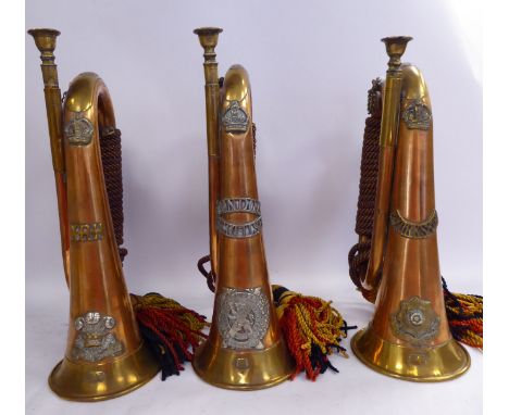 Three similar copper and brass military bugles with corded tassles, variously mounted with insignia, engraved/impressed detai