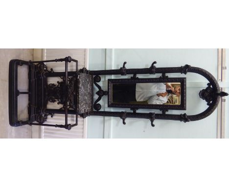 A late Victorian black painted, elaborately cast iron hallstand, the round arched top incorporating a central, rectangular mi