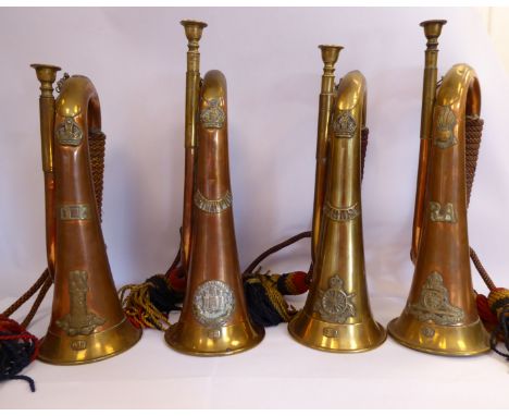 Three similar copper and brass military bugles and another brass with corded tassles, variously mounted with insignia, engrav