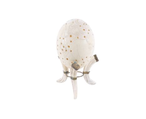A carved and signed ostrich egg on boar tusk and brass stand. The egg carved with African wildlife and signed by the artist '