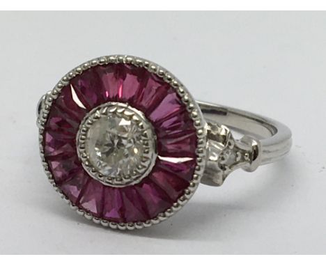 A platinum ruby and diamond target style ring, set with a central diamond and a halo of calibre- cut rubies, with further dia