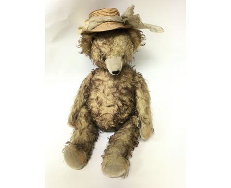 A large vintage plush teddy bear with long arms and straw hat and growler