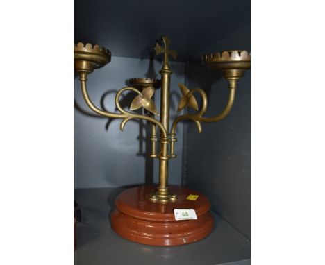 An arts and crafts brass candlestick holder having three swinging arms with ivy decoration and cross to top, mounted on ceram