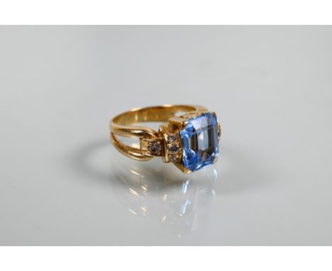 A Continental ring, the central rectangular blue topaz with white paste set shoulders in high claw setting, yellow metal set 