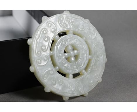 A Chinese pale celadon jade dharmachakra (wheel of dharma) Buddhist amulet or pendant, with central hub, two c-scroll decorat