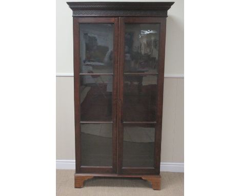 A Georgian mahogany Bookcase with Greek key and surface fret carved cornice above a pair of glazed doors enclosing shelves on