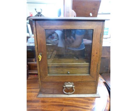 An oak smokers cabinet with pipe rack, two drawers below, main glazed door and plaque to top dated 1928