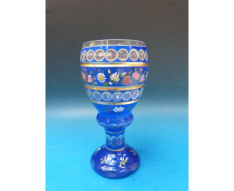 A Bohemian double overlaid cut glass goblet with floral enamel decoration and gilt banding to the cut sections 18.5cm tall. 