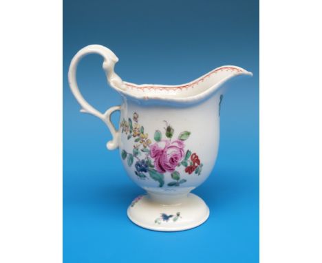 An 18thC Liverpool helmet-shaped pedestal cream jug painted in coloured enamels with flowers and leaves, and with a looped bi