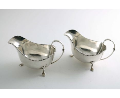A PAIR OF EARLY 20TH CENTURY SAUCE BOATS on three feet with bobbin borders &amp; loop handles by Walker &amp; Hall, Sheffield