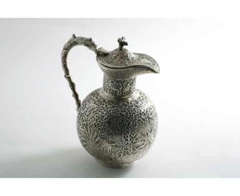 A LATE 19TH CENTURY INDIAN BULBOUS JUG with a hinged cover, ram's mask finial and a naturalistic handle, the whole chased wit