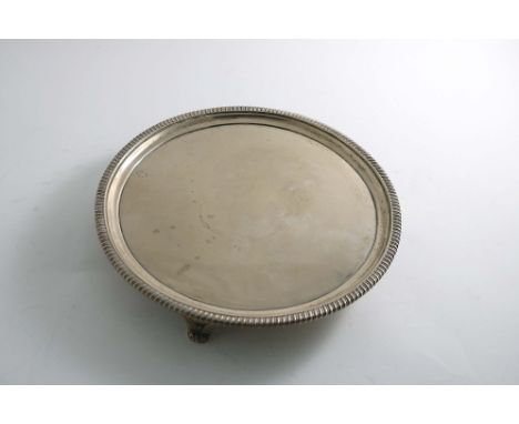 A GEORGE III CIRCULAR SALVER with a gadrooned border and gadrooned bracket feet, by John Mewburn, London 1807; 9.1"  (23.2 cm