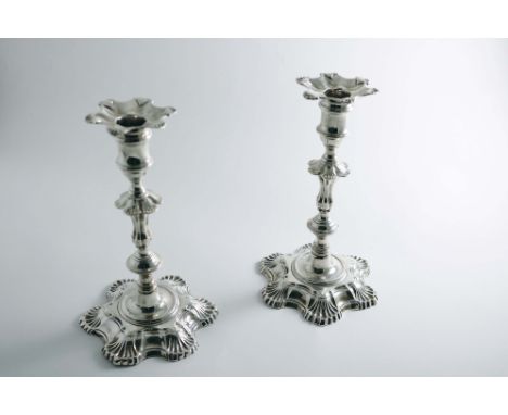 TWO VERY SIMILAR GEORGE II / III CAST CANDLESTICKS on hexafoil bases with knopped columns, shell decoration and spool-shaped 