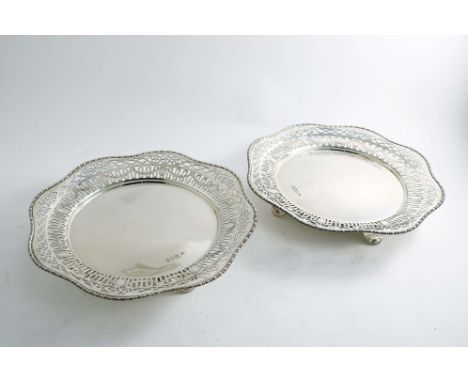 A PAIR OF EARLY 20TH CENTURY DESSERT DISHES with a shaped circular outline, pierced borders and scroll bracket feet, by Charl