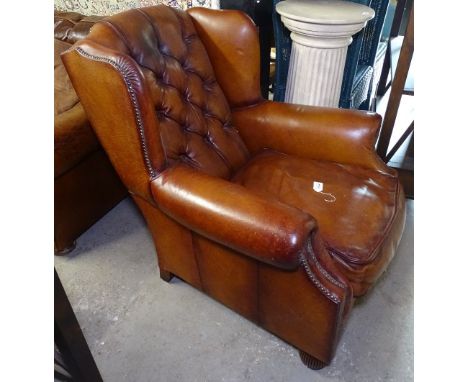 A good quality button-back and brass studded leather upholstered wingback armchair, with matching footstool, raised on melon 