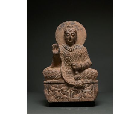 100 – 300 AD. Gandhara. Seated schist figure of Buddha atop a square platform ornamented with floral motifs. The facial featu