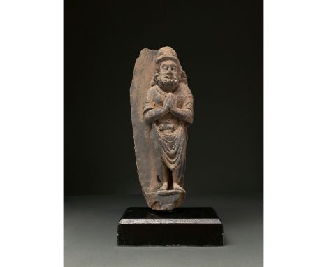 100-300 AD. Gandharan. Schist figure of a standing worshipper in high relief. He holds his hands in front of him, with his pa