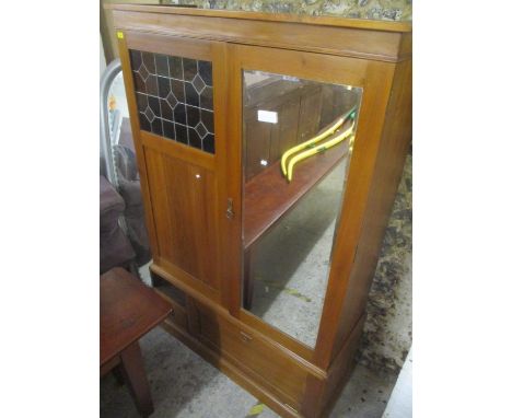 An Arts and Crafts pine two door wardrobe having stained glass and mirrored door above an open shelf, drawer and fall flap do