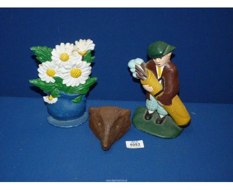 A cast metal doorstop modelled as a golf caddy, 8" long, another of daisies in vase, 8 1/2" long and a cast iron hedgehog mas