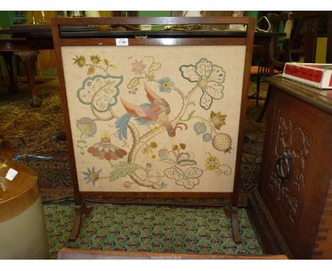 A wooden framed fire screen with wool embroidered panel depicting and exotic bird perching on a branch with stylised flowers.