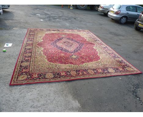 A large bordered and patterned Wilton Carpet in red, yellow and navy ground, with all over floral design, (one cut mark to ed