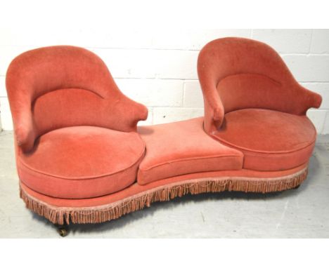 An early 20th century pink-upholstered conversation sofa, with two swivel tub chairs on turned mahogany legs and brass castor