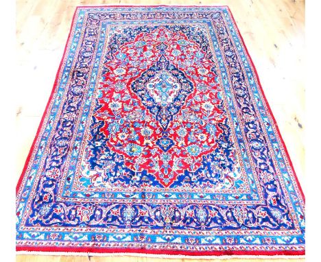 A fine Central Persian Kashan carpet, having a medallion on a red field with blue and ivory spandrels, surrounded by one frie