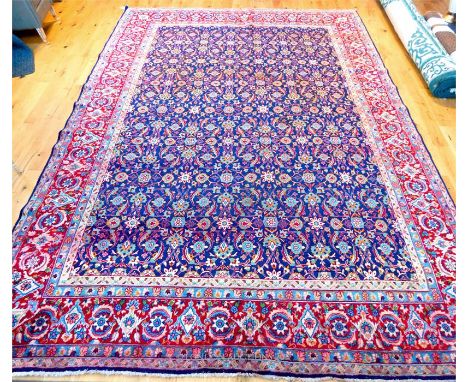 A large Kashan carpet, having floral designs on a midnight blue field, surrounded by one red frieze border and four running b
