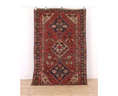 A tribal wool rug, 20th century, Caucasian, woven with geometric medallions and flowerheads to a red ground, 208 x 130cmCondi