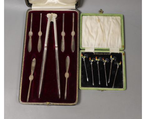 A George V cased set of six silver lobster picks and plated crackers and a similar set of silver and enamel cocktail sticks