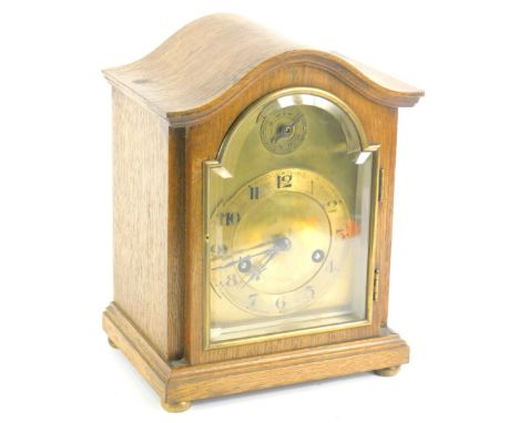 An early 20thC oak mantel clock, with a bevelled glass arched door, and arched brass dial, Arabic numerals on bun feet, 25cm 