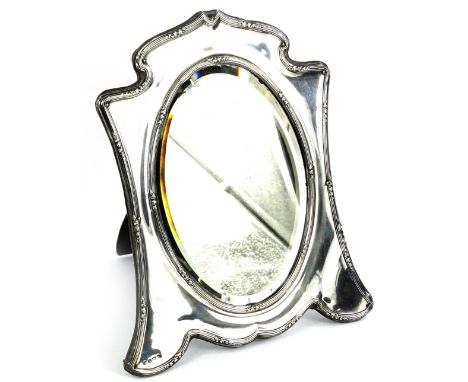 An Edwardian silver dressing mirror, the oval plate with a bevel edge, the frame decorated with reeded bands etc., Birmingham